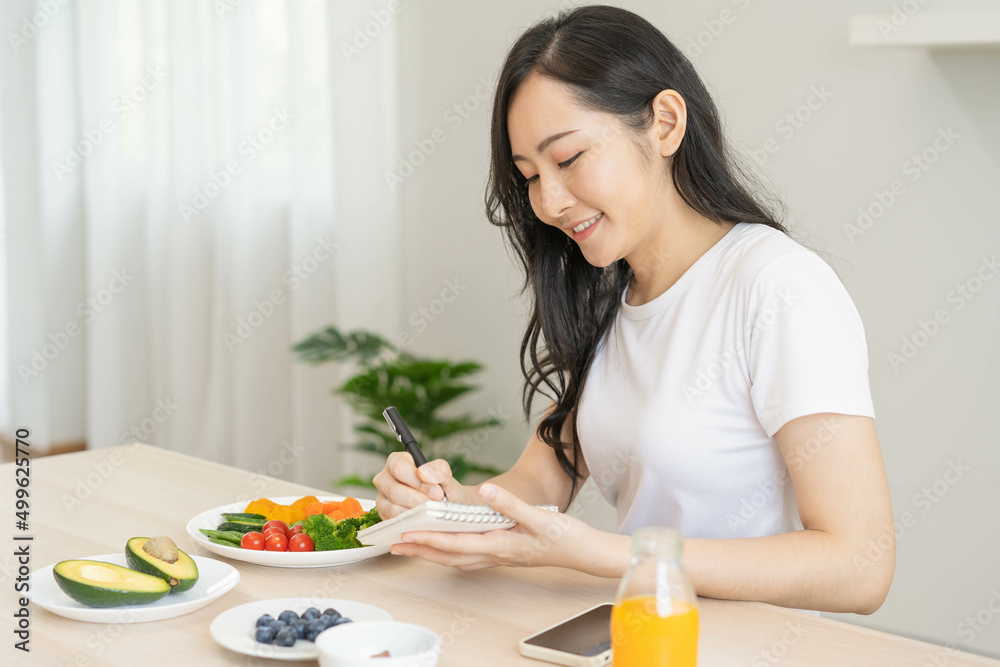 Diet, Dieting asian young woman write diet plan right nutrition on table with fresh vegetables salad, almond is different food ingredients in green. Nutritionist of healthy, nutrition of weight loss. Diet, Dieting asian young woman write diet plan right nutrition on table with fresh vegetables salad, almond is different food ingredients in green. Nutritionist of healthy, nutrition of weight loss.