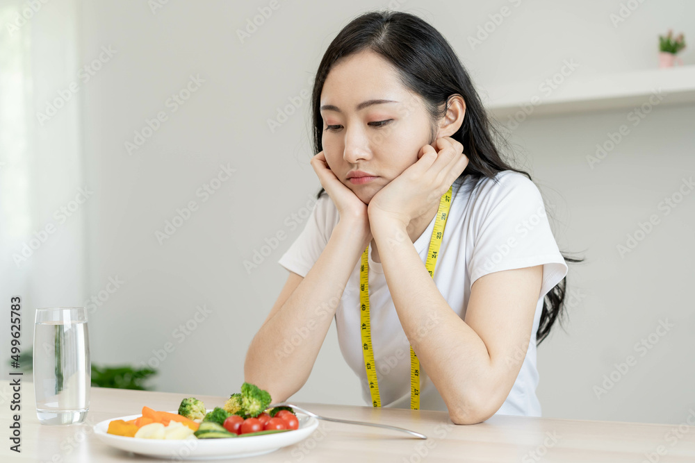 Diet in bored face, unhappy beautiful asian young woman on dieting, looking at salad plate on table, dislike or tired with eat fresh vegetables. Nutritionist of healthy, nutrition of weight loss. Diet in bored face, unhappy beautiful asian young woman on dieting, looking at salad plate on table, dislike or tired with eat fresh vegetables. Nutritionist of healthy, nutrition of weight loss.