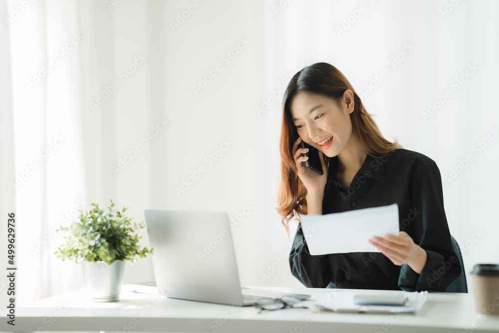 Asian businesswoman in formal suit in office happy and cheerful during using smartphone and working with financial report. Asian businesswoman in formal suit in office happy and cheerful during using smartphone and working with financial report.