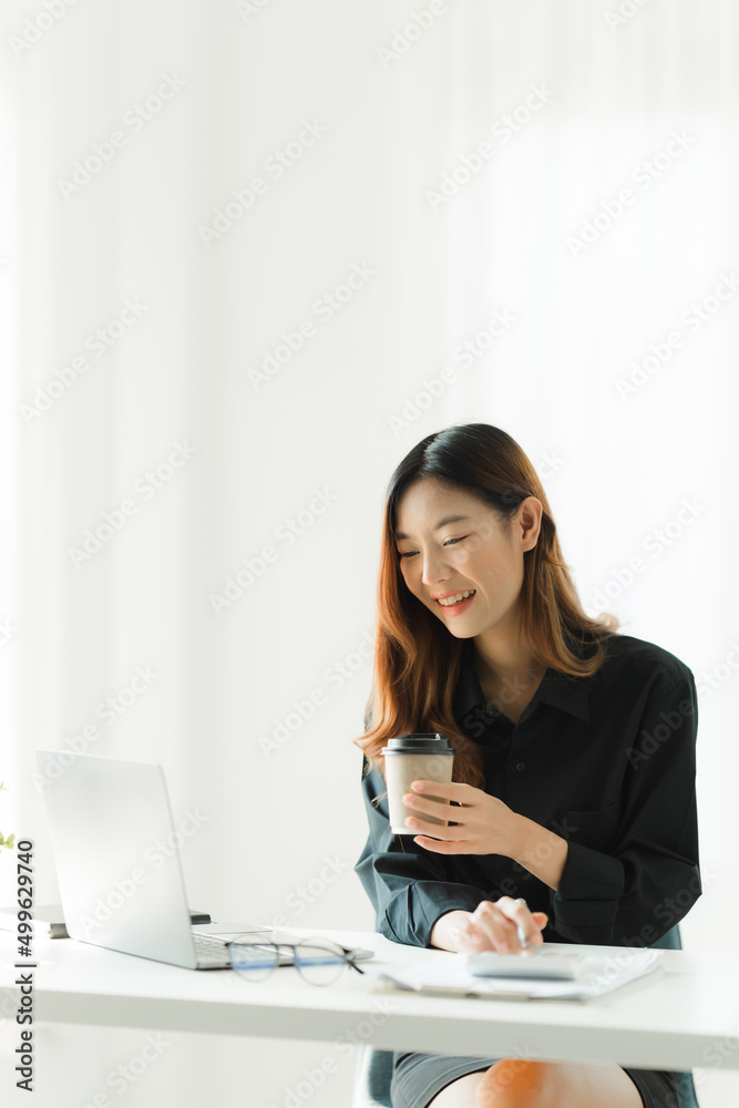 Beautiful young asian business woman drinking coffee and using laptop computer while working in office. Beautiful young asian business woman drinking coffee and using laptop computer while working in office.