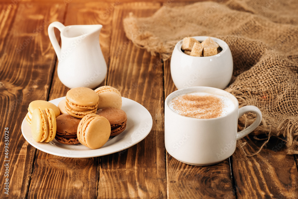 Obraz premium cup of coffee, milk, sugar and macaroons on wooden background