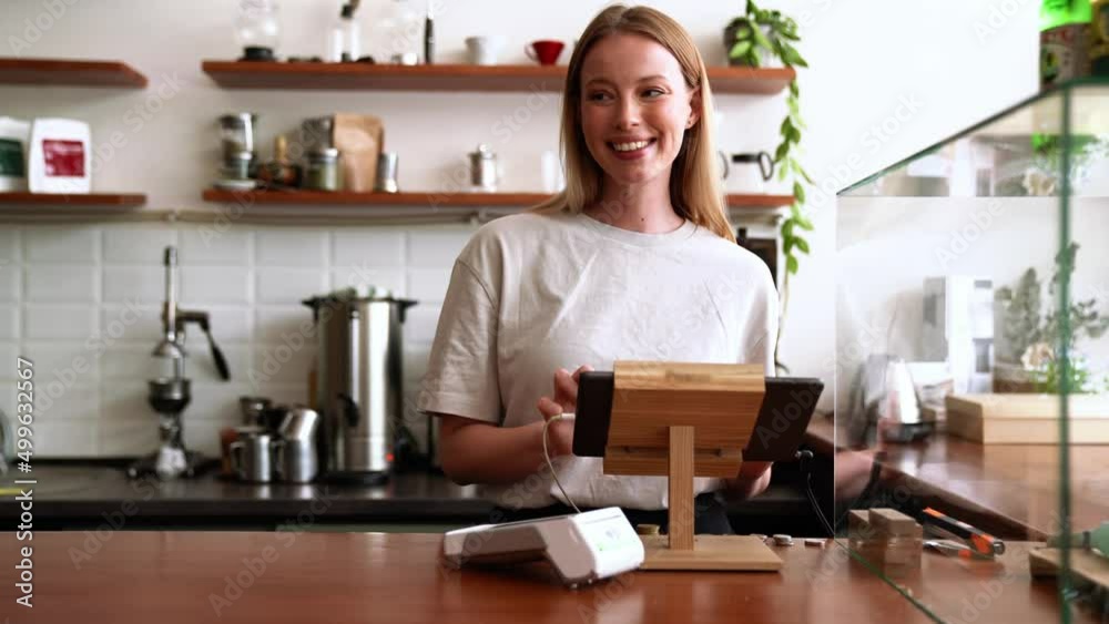 Smiling blonde woman barista punches the order at the checkout in the cafe Smiling blonde woman barista punches the order at the checkout in the cafe