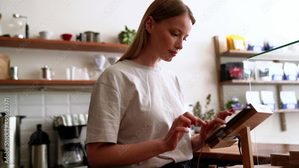 Pretty blonde woman barista punches the order at the checkout in the cafe Pretty blonde woman barista punches the order at the checkout in the cafe