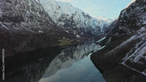 Beautiful aerial flying in unesco listed Naeroyfjord towards Gudvangen - Snow capped tall mountains and mirror like reflections in water surface photo