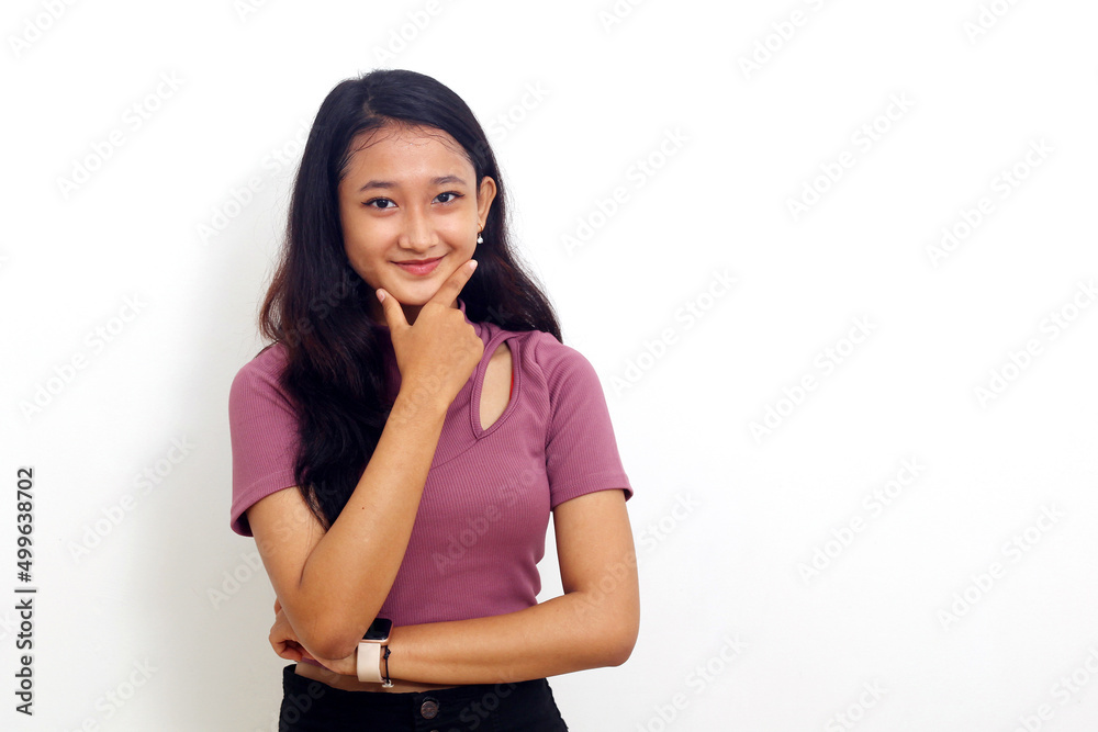 Full length view of pensive young woman standing with hand on chin and looking at camera on white Full length view of pensive young woman standing with hand on chin and looking at camera on white