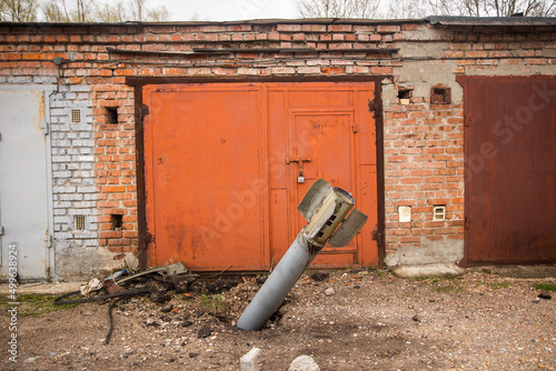 Close-up view stock image of real unexploded military missile, torpedo or shell stuck in ground near doors of garages outdoors. Moments of dreadful war of Russia against Ukraine in 2022