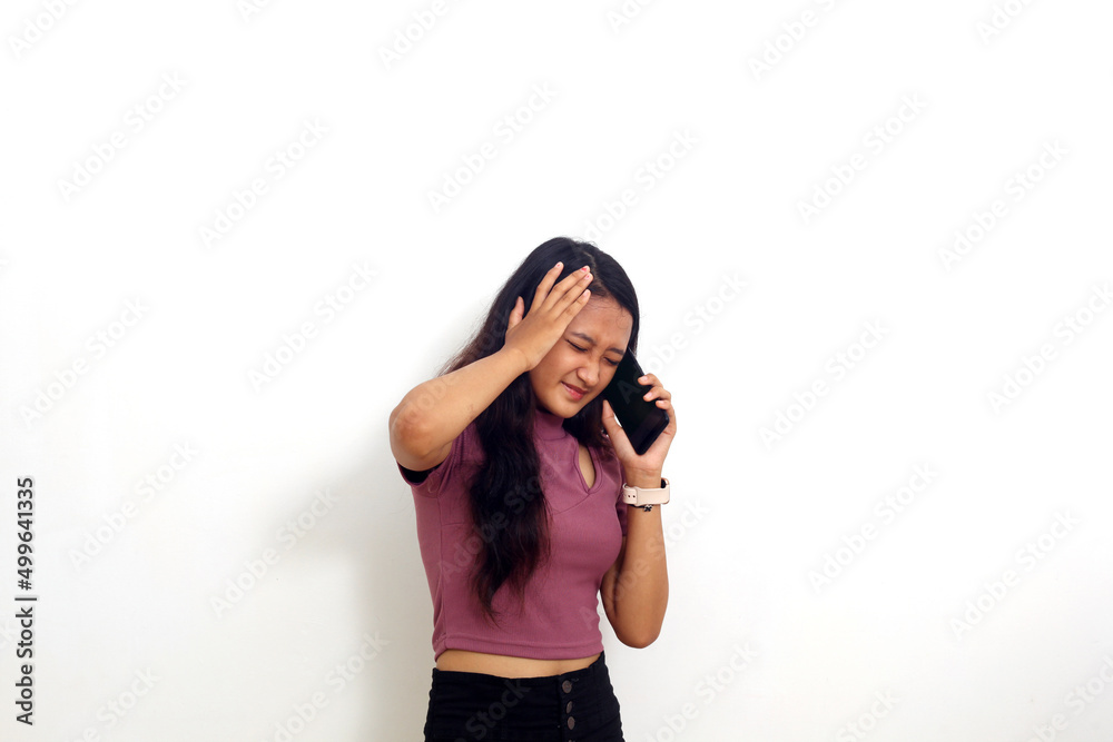 Stressed young asian girl standing while talking on a phone. Isolated on white background Stressed young asian girl standing while talking on a phone. Isolated on white background