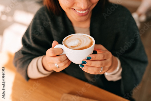 Top view photo of smiling adorable lady with wonderful smile, dark manicure is holding coffee and enjoying resting in cafeteria