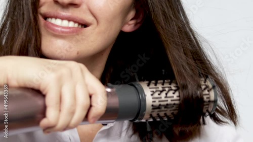 young woman using a modern rotative hair brush to style her hair. smiling girl, close up slow motion video. hair dryer and volumizer. Thermal and ceramic coating of dryer. photo