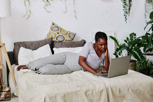 African woman using her laptop while lying on bed and talking to her doctor online photo