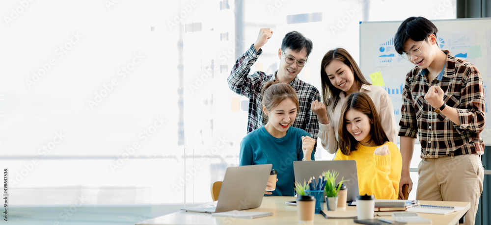 A group of startup company employees are in the conference room, raising their hands to show their appreciation after looking at the company's sales and profitable results. Startup company concept.