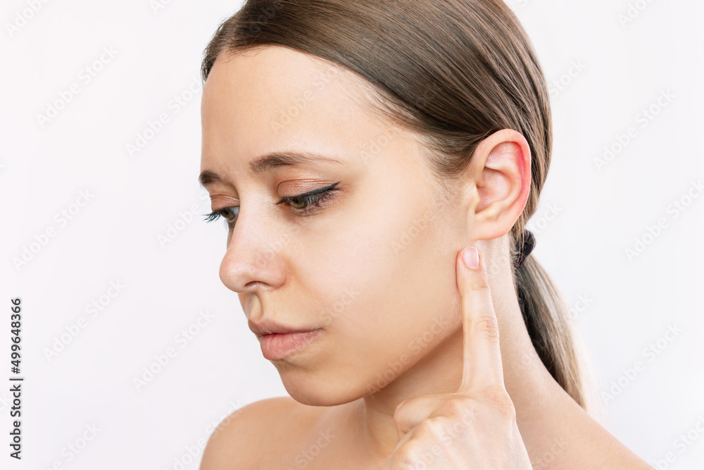 Portait of a young caucasian woman pointing at her ear with her finger isolated on a white background. Correction of auricles, otoplasty