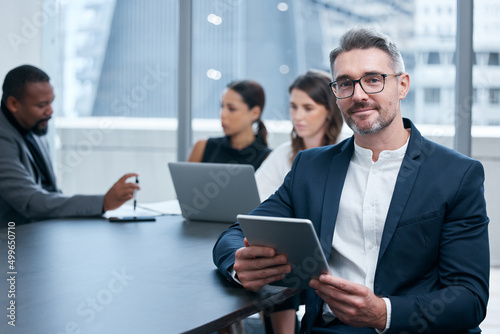 Were always busy making big things happen here. Portrait of a mature businessman using a digital tablet in an office with his colleagues in the background. photo