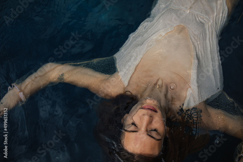 Meditating young woman floating in ocean water with arms outstretched photo