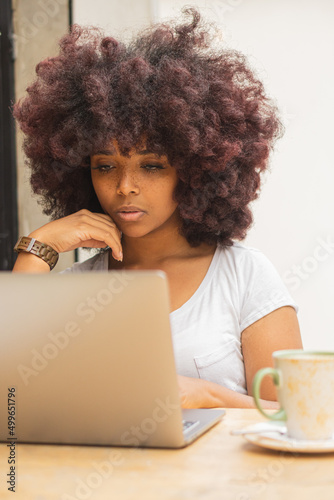 Young Afro woman in a coffee shop working online at her computer. photo