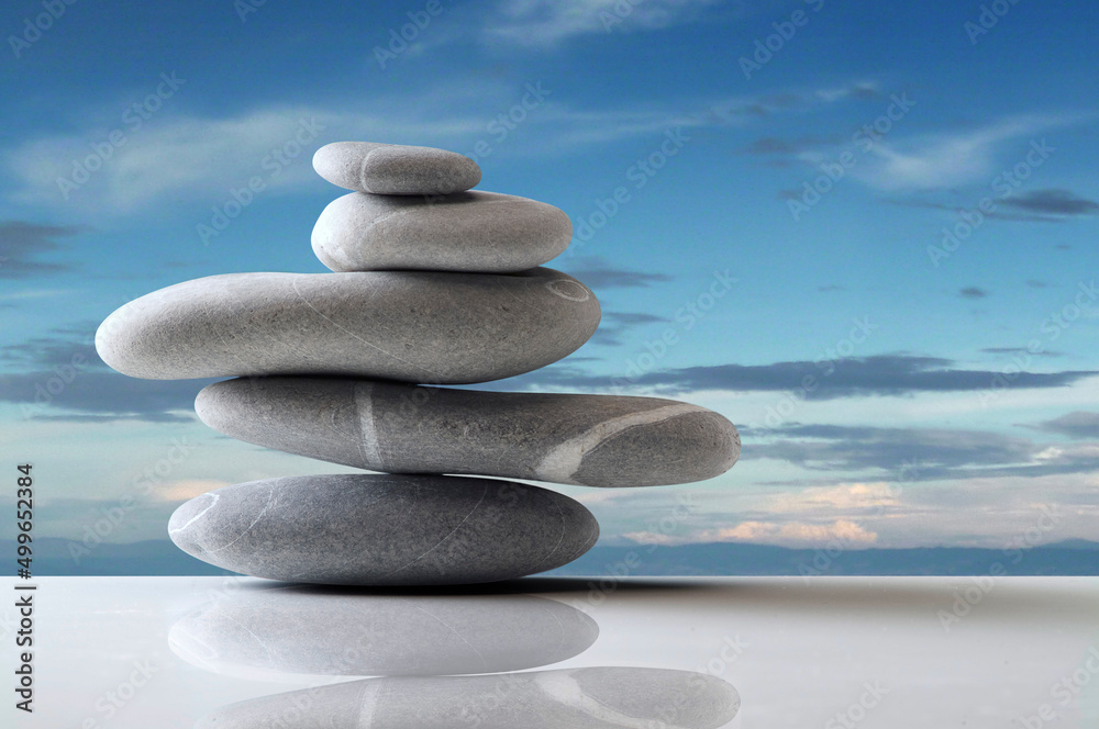 five grey stones balanced over white surface over blue sky
