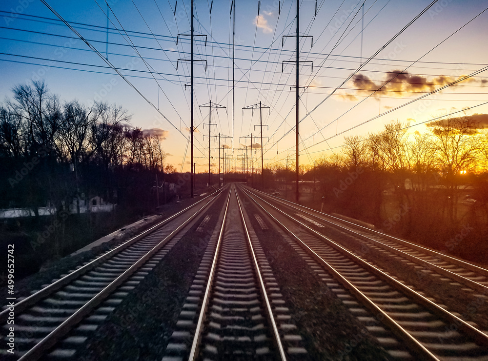 Train tracks converging on the horizon landscape with colorful sunset light in the background sky