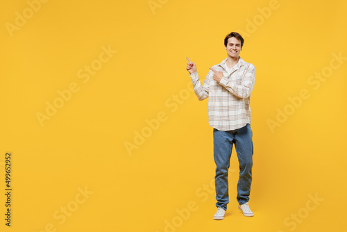 Full body young smiling happy cheerful fun man 20s wearing white casual shirt point index finger aside on workspace area isolated on plain yellow background studio portrait. People lifestyle concept.