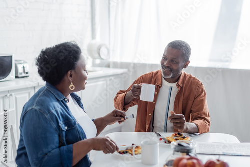 smiling african american man talking with senior wife during breakfast.
