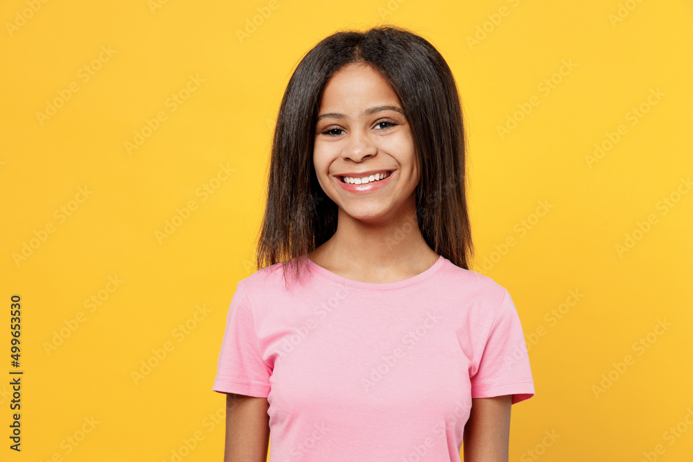 Little smiling happy cheerful fun kid girl of African American ethnicity 12-13 years old in pink t-shirt look camera isolated on plain yellow background studio portrait. Childhood lifestyle concept. Little smiling happy cheerful fun kid girl of African American ethnicity 12-13 years old in pink t-shirt look camera isolated on plain yellow background studio portrait. Childhood lifestyle concept.