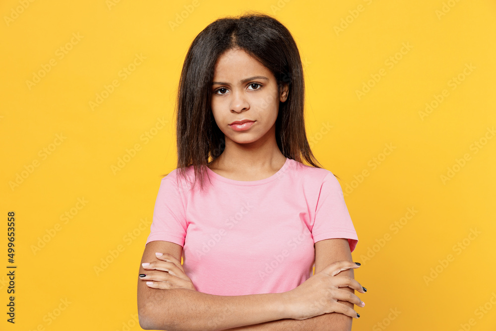 Little depressed sad kid girl of African American ethnicity 12-13 year old in pink t-shirt hold hands crossed folded look camera isolated on plain yellow background studio Childhood lifestyle concept Little depressed sad kid girl of African American ethnicity 12-13 year old in pink t-shirt hold hands crossed folded look camera isolated on plain yellow background studio Childhood lifestyle concept