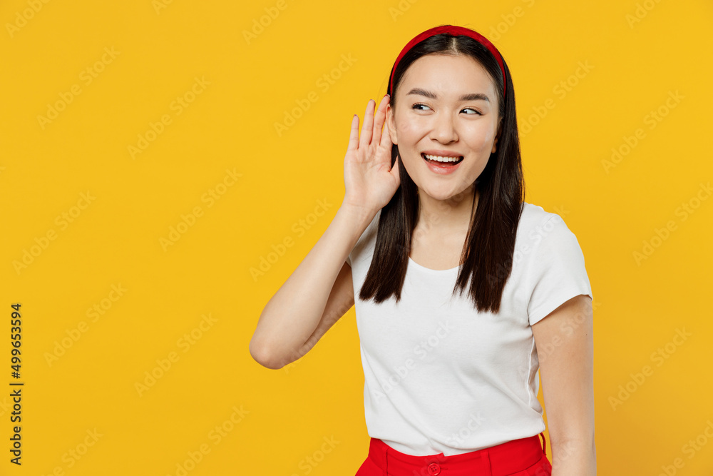 Curious young girl woman of Asian ethnicity 20s in white t-shirt try to hear you overhear listening intently isolated on plain yellow background studio portrait. People emotions lifestyle concept Curious young girl woman of Asian ethnicity 20s in white t-shirt try to hear you overhear listening intently isolated on plain yellow background studio portrait. People emotions lifestyle concept