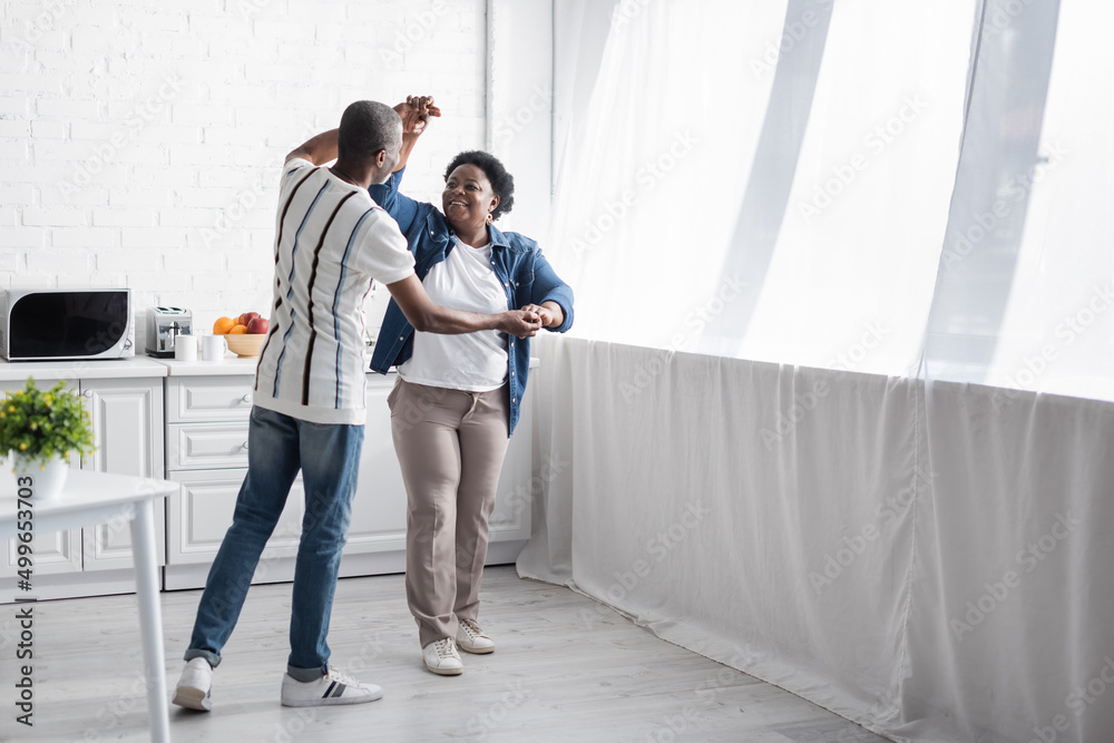 full length of cheerful senior african american couple dancing in kitchen.