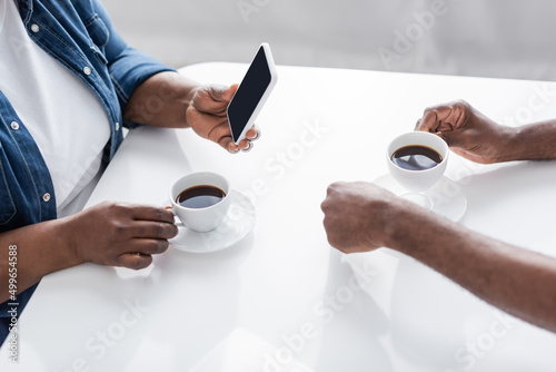 cropped view of senior african american woman holding smartphone near husband and cups on table.