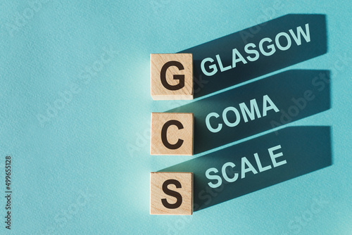 Konstfotografi GCS Glasgow Coma Scale text, written on wooden blocks with shadows on blue background