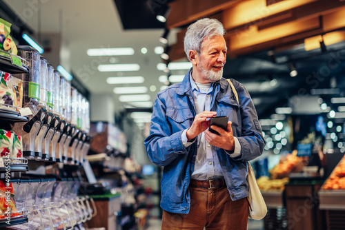 Smiling senior man using phone in grocery store © bernardbodo