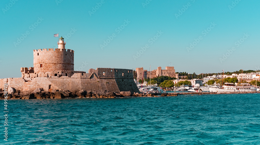 Rhodes Mandraki Port, Rhodes Island, Greece - 05 July 2021: Entrance to Rhodes Old Harbour, Castle fortress of St. Nicolas, Lighthouse, view from sea, former place of Colossus of Rhodes