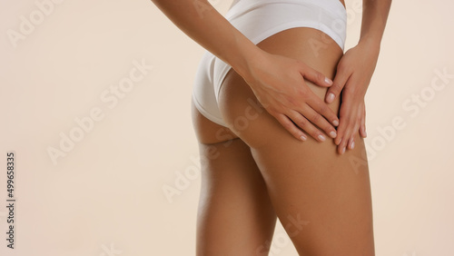 Close up shot of slim African American woman touches her elastic skin on hips against beige background | body care concept
