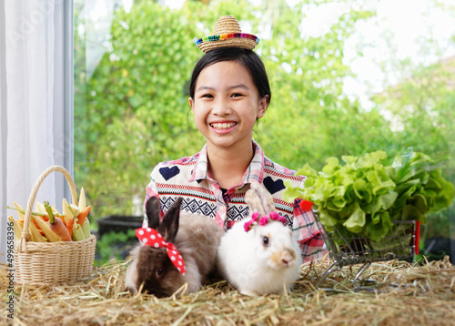a little pretty farmer girl in wear a little cute hat smiling with two rabbits and vegetables in a basket and a shopping cart selective focus at a girl