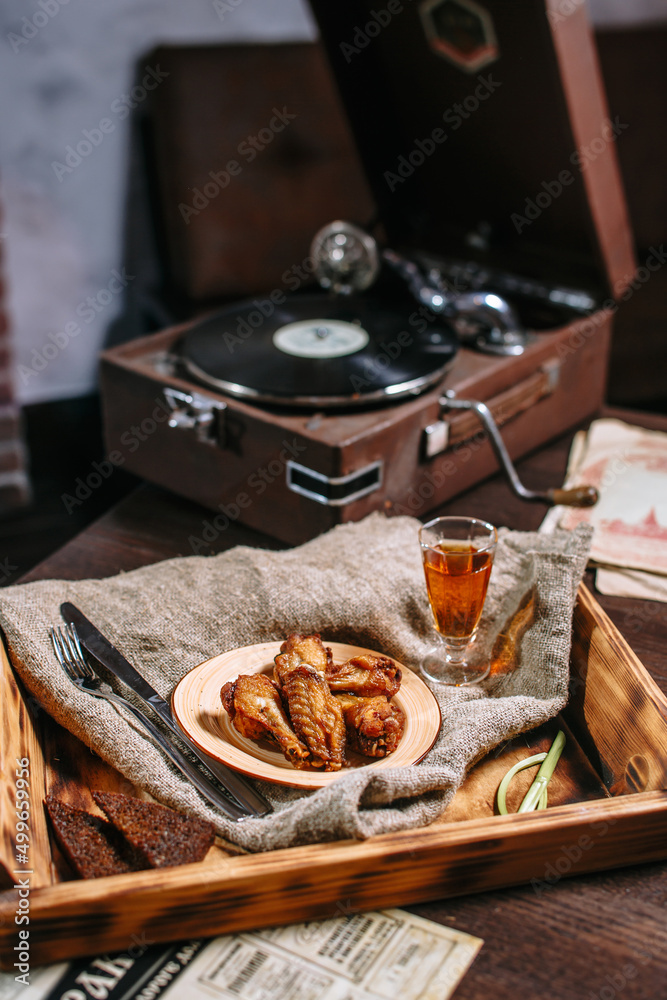 Fried chicken wings on a plate in a tavern. There is a stack of moonshine next to it. Post-war still life with gramophone Fried chicken wings on a plate in a tavern. There is a stack of moonshine next to it. Post-war still life with gramophone