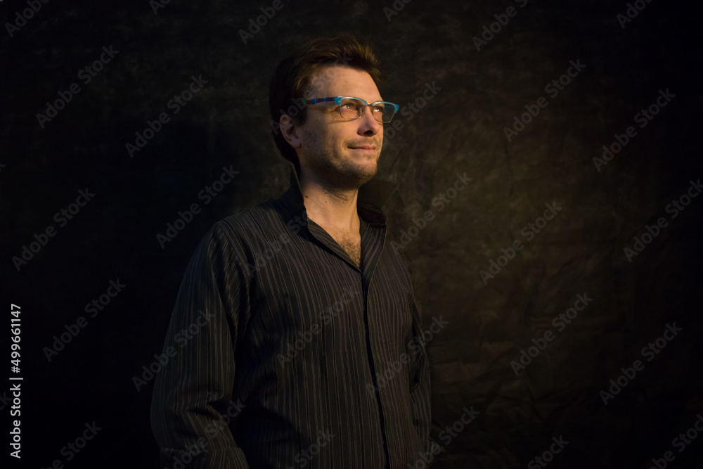 Retrato de hombre joven con camisa oscura y  anteojos azules en fondo negro. Bodegón. Naturaleza muerta. Joven caucásico.