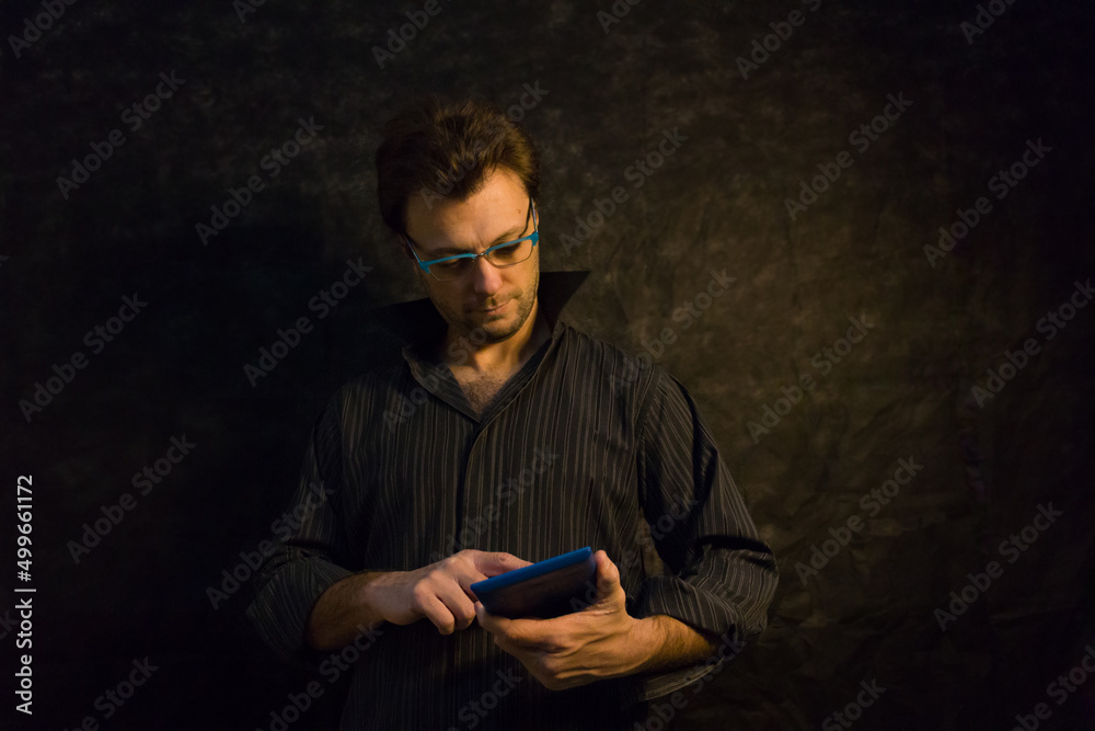 Retrato de hombre joven con camisa oscura, anteojos azules y tablet azul sobre fondo negro. Bodegón. Naturaleza muerta.	Tecnología. Joven caucásico.