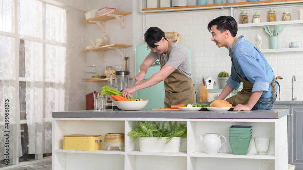 Young smiling gay couple cooking together in the kitchen at home, LGBTQ and diversity concept.