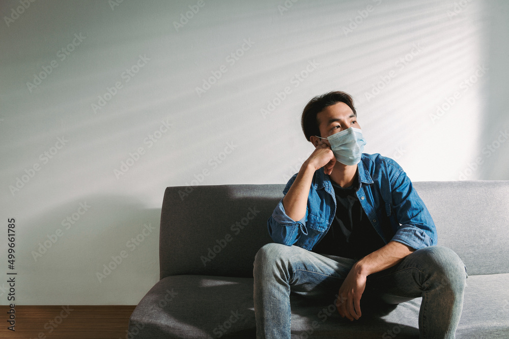 An upset health problem Asian patient man wearing a face mask at home or hospital alone sad and waiting for a doctor. Hospital and Health care during Coronavirus or Covid-19 quarantine concept