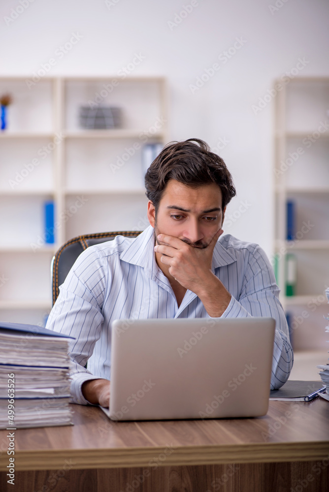 Young male employee unhappy with excessive work in the office Young male employee unhappy with excessive work in the office