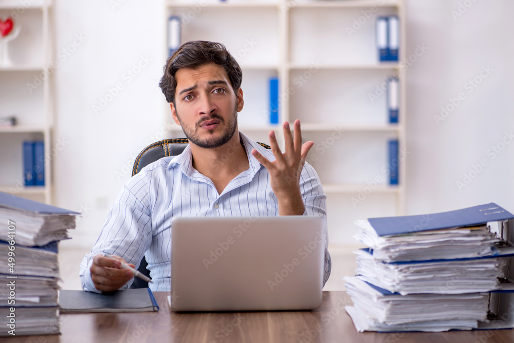 Young male employee unhappy with excessive work in the office Young male employee unhappy with excessive work in the office