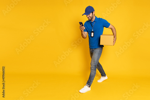 Delivery man holding parcel box and mobile phone and walking isolated on yellow background, Online shopping shipping and fast express delivery service concept