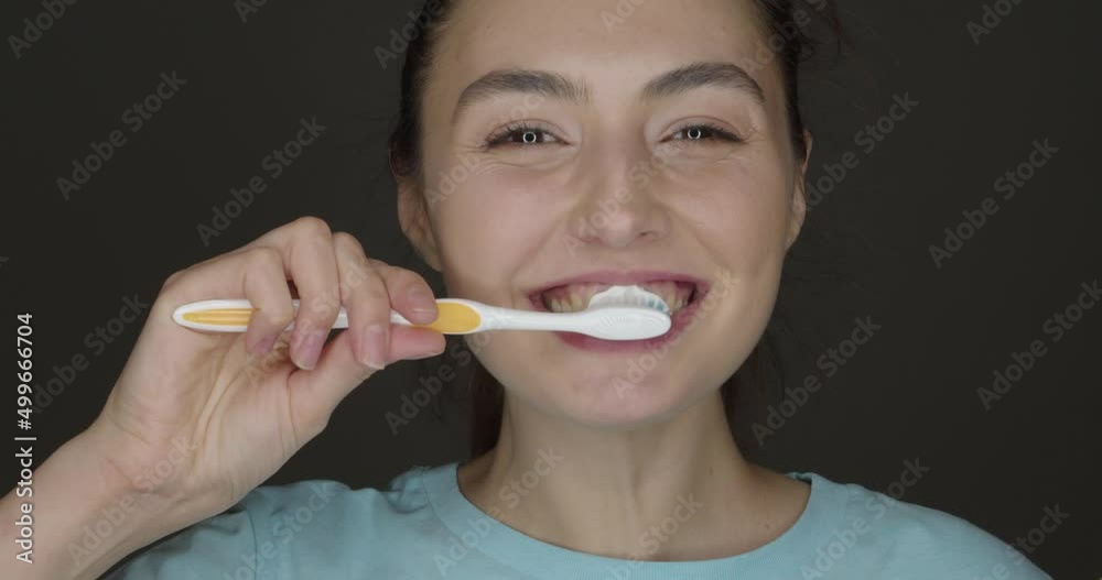 Happy young woman brushing teeth on dark background Happy young woman brushing teeth on dark background