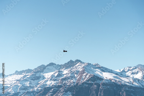 Horizontal shot of Andean condor flying in profile over snow-capped Andes mountains, Chile.snow
