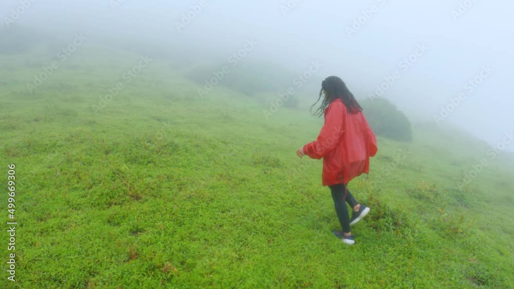 Indian woman walking on green mountain in Monsoon. Landscape with young woman, foggy hills, forest, sky. Hiking in the Western Ghats, India Indian woman walking on green mountain in Monsoon. Landscape with young woman, foggy hills, forest, sky. Hiking in the Western Ghats, India