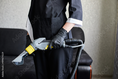 Close up of female housekeeper arm cleaning sofa with washing vacuum cleaner . Cleaning service company employee removing dirt from furniture in flat with professional equipment © bondvit