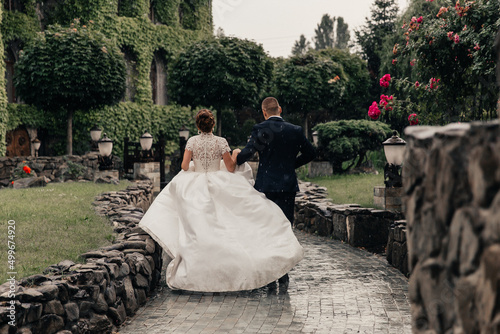 the bride and groom in a lush white dress running in the rain against the backdrop of a beautiful building overgrown with ivy