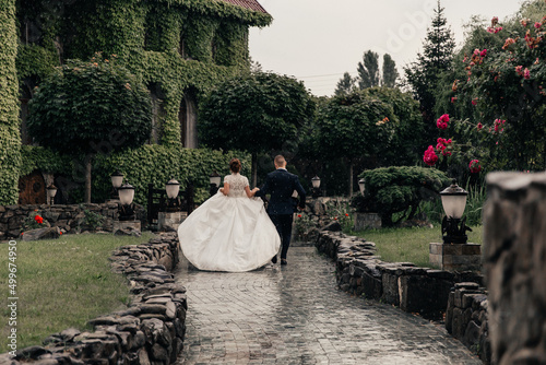 the bride and groom in a lush white dress running in the rain against the backdrop of a beautiful building overgrown with ivy