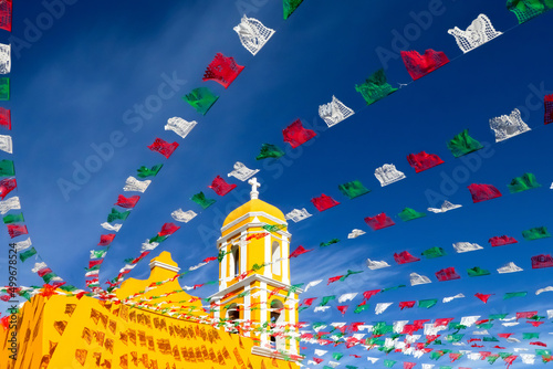 Yellow Catholic Church and holiday flags against a blue sky. Mexico. Old city of Izamal. photo