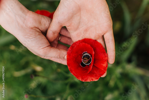 young couple holding a red poppy flower in the heart of which are engagement rings