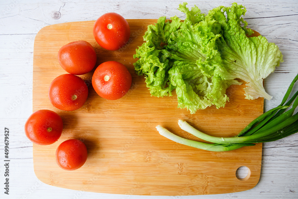 Fresh vegetables for salad lie on a wooden table with a cutting board. Top view. Close-up. Fresh vegetables for salad lie on a wooden table with a cutting board. Top view. Close-up.